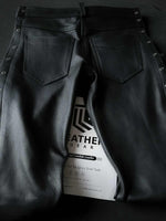 Lade das Bild in den Galerie-Viewer, Flat lay of the back of side-laced black leather pants showing pocket placement and ass contour built for fetish and biker scenes.
