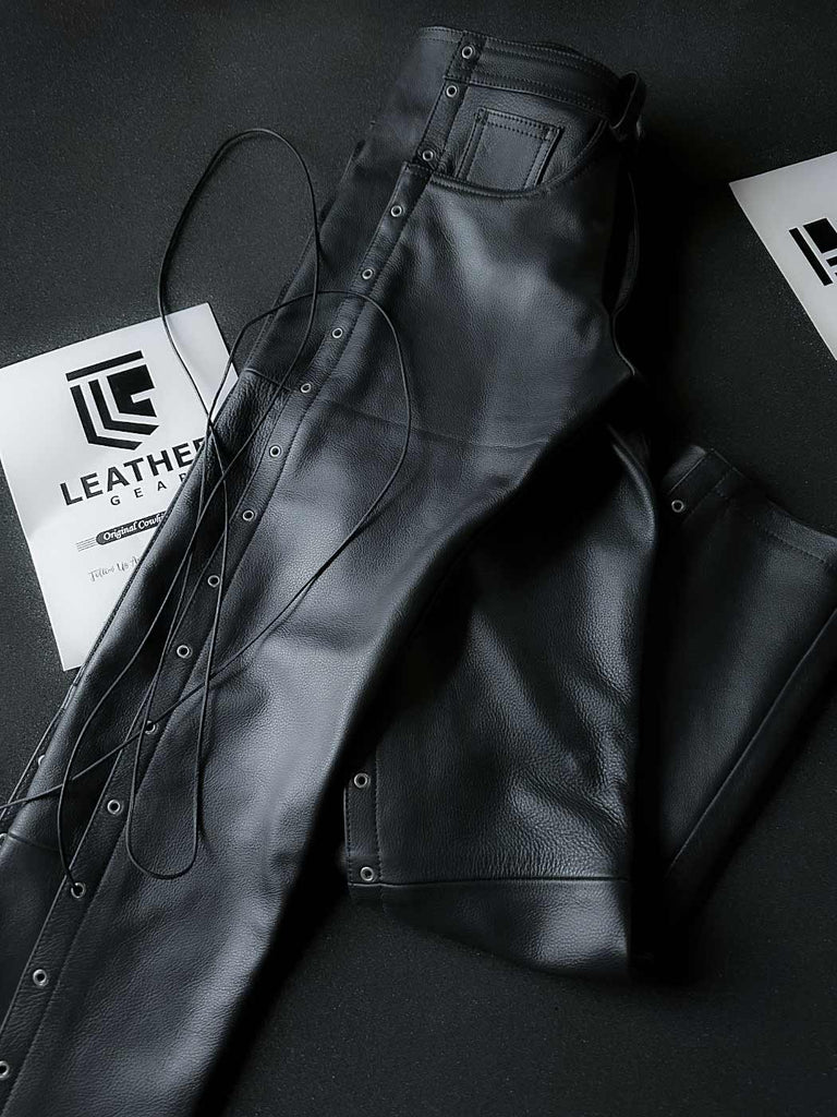 Side-folded black leather biker pants laid flat, showcasing cowhide finish and lace-up detailing for gay leather gear collectors.