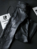 Lade das Bild in den Galerie-Viewer, Side-folded black leather biker pants laid flat, showcasing cowhide finish and lace-up detailing for gay leather gear collectors.

