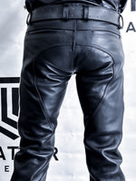 Charger l'image dans la galerie, Black leather pants on a person against a gray background with a brand logo.
