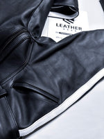 Charger l'image dans la galerie, Close-up of a black leather jacket with a visible brand label on a white background
